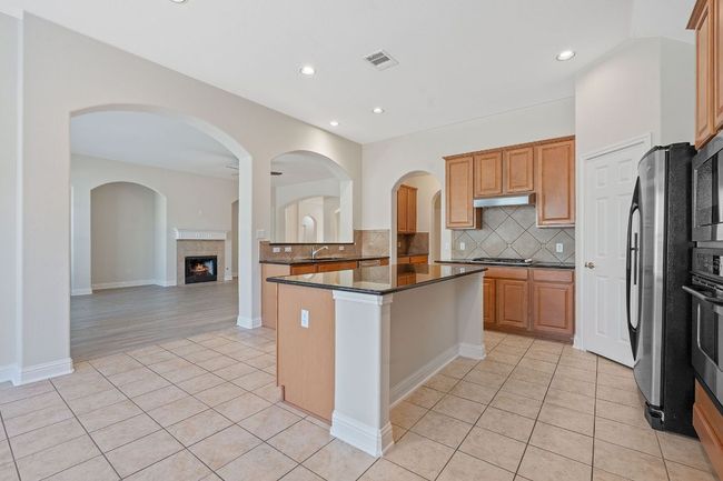 Kitchen featuring light tile patterned flooring, stainless steel appliances, a tiled fireplace, tasteful backsplash, and under cabinet range hood | Image 12