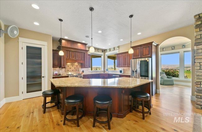 Kitchen featuring stainless steel refrigerator with ice dispenser, decorative backsplash, a large island, light wood-type flooring, and arched walkways | Image 10