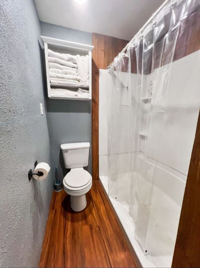 Full bathroom featuring a shower stall, toilet, a textured wall, and wood finished floors | Image 9