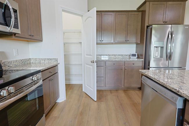 Kitchen with stainless steel appliances, light wood-style flooring, light stone countertops, and dark brown cabinetry | Image 7