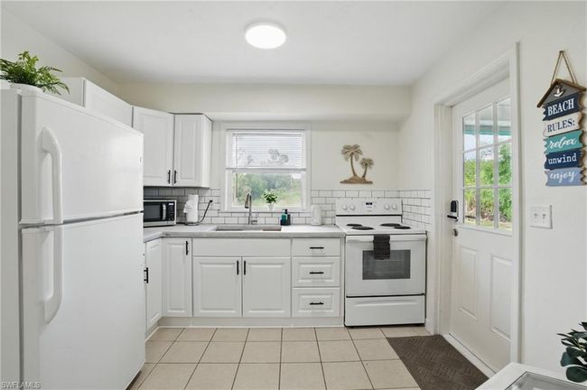 Kitchen featuring white appliances, light tile patterned flooring, decorative backsplash, light countertops, and white cabinets | Image 21