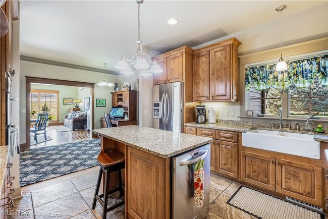 Kitchen with a kitchen island, light granite counters, hanging light fixtures, stainless steel appliances, and a farm sink | Image 25