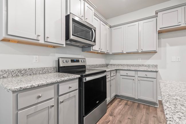 Kitchen with appliances with stainless steel finishes, wood finished floors, gray cabinets, and light stone counters | Image 16