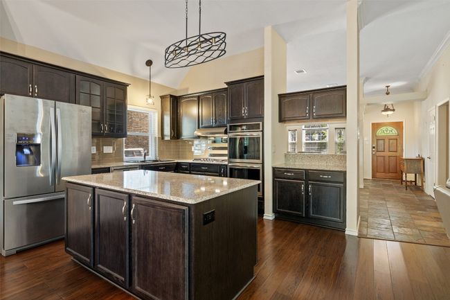 Kitchen with appliances with stainless steel finishes, dark brown cabinets, a center island, a sink, and under cabinet range hood | Image 18