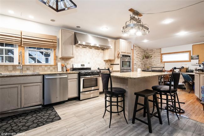Kitchen with tasteful backsplash, a sink, wall chimney range hood, light wood-style flooring, and appliances with stainless steel finishes | Image 8