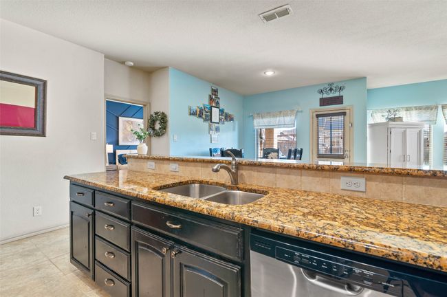 Kitchen featuring light stone counters, a sink, visible vents, stainless steel dishwasher, and dark cabinetry | Image 15
