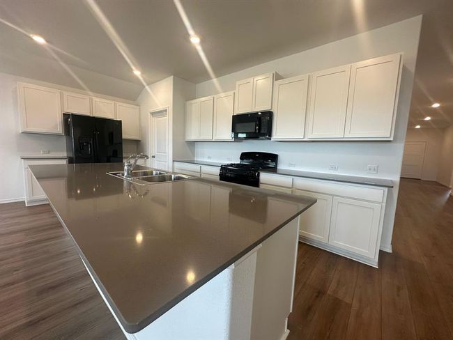 Kitchen featuring black appliances, a sink, a large island, white cabinets, and vaulted ceiling | Image 15