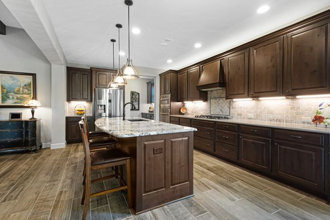 Kitchen with custom exhaust hood, a sink, wood finished floors, dark brown cabinets, and recessed lighting | Image 12