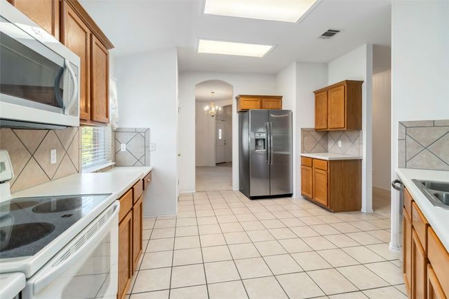 Kitchen with white appliances, arched walkways, brown cabinetry, and backsplash | Image 16