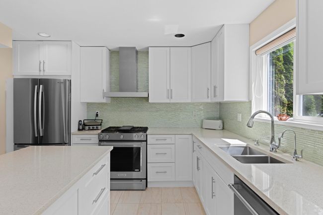 Kitchen with appliances with stainless steel finishes, wall chimney range hood, white cabinetry, light stone counters, and decorative backsplash | Image 11