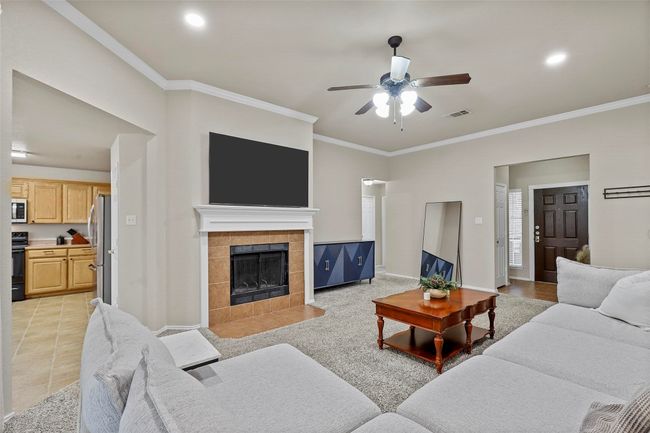 Living area featuring baseboards, visible vents, a tile fireplace, ceiling fan, and crown molding | Image 5