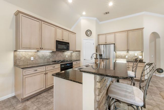 Kitchen featuring black appliances, arched walkways, an island with sink, crown molding, and backsplash | Image 16