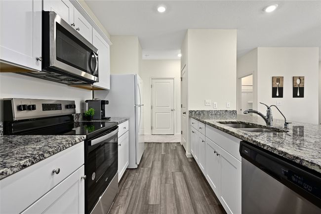 Kitchen with dark stone counters, a sink, stainless steel appliances, white cabinetry, and dark wood-style flooring | Image 19