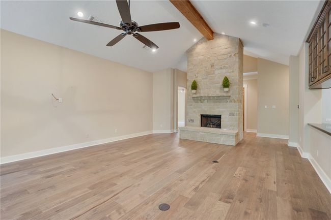 Unfurnished living room with ceiling fan, light wood-style flooring, a stone fireplace, baseboards, and recessed lighting | Image 5