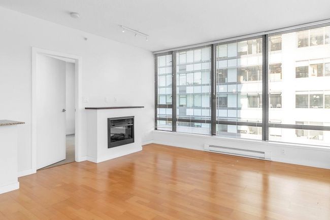 Unfurnished living room with a baseboard heating unit, light wood-style floors, rail lighting, and a glass covered fireplace | Image 11