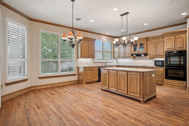 Kitchen with a chandelier, double ovens, crown molding, hardwood flooring, and a center island. | Image 13