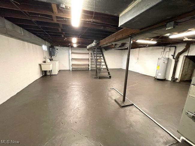 Unfinished below grade area with electric water heater, washer / clothes dryer, a sink, and electric panel | Image 5