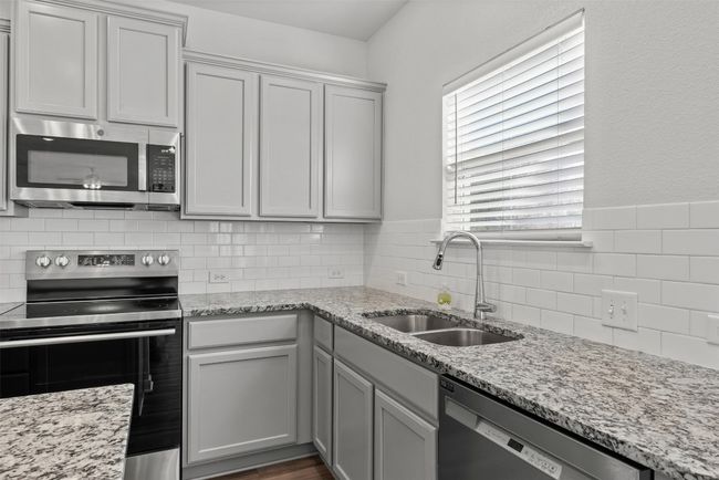 Kitchen with appliances with stainless steel finishes, backsplash, and light stone counters | Image 15