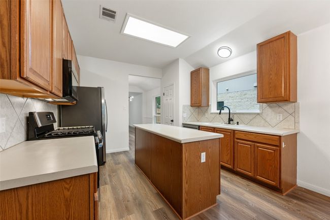 Kitchen with a center island, black microwave, backsplash, brown cabinets, and vaulted ceiling | Image 20