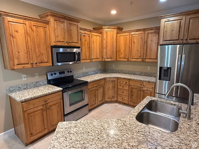 Kitchen featuring stainless steel appliances, a sink, crown molding, brown cabinetry, and light tile patterned floors | Image 4