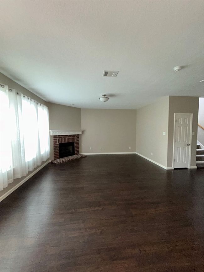 Unfurnished living room featuring dark wood-style floors, baseboards, a brick fireplace, and stairway | Image 20