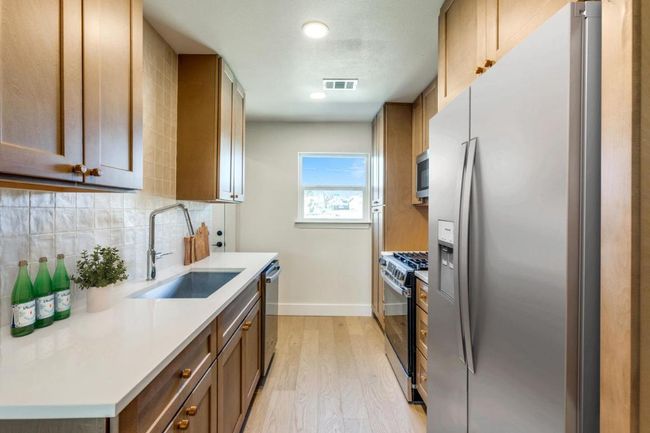 Kitchen featuring stainless steel appliances, a sink, visible vents, light wood-type flooring, and backsplash | Image 14