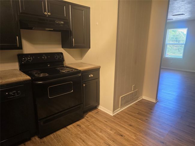 Kitchen featuring black appliances, under cabinet range hood, light wood-style flooring, and light countertops | Image 8