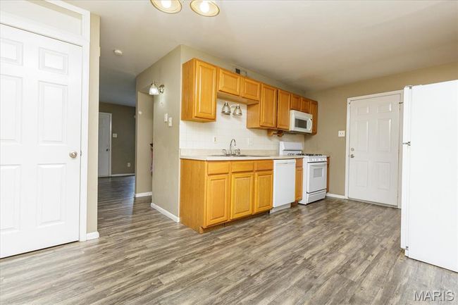 Kitchen with white appliances, wood finished floors, light countertops, and backsplash | Image 6