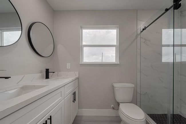 Stylish and serene, this bath features a glass-enclosed shower with full-height tilework, a dual-sink vanity with black fixtures, and a window that fills the space with natural light. | Image 17