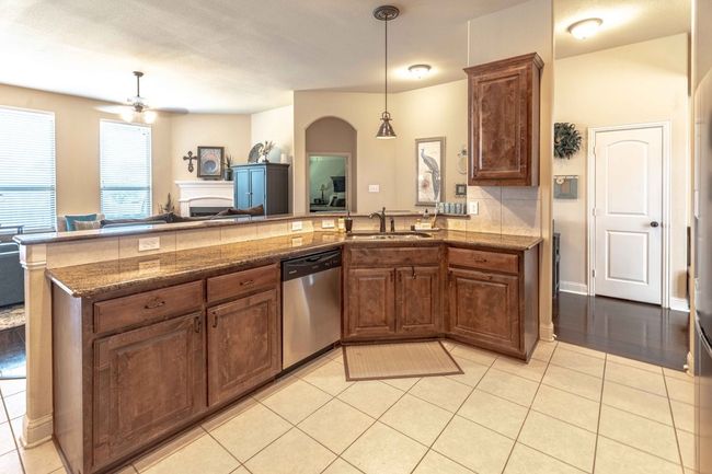 Kitchen featuring dishwasher, ceiling fan, a fireplace, a peninsula, and light tile patterned flooring | Image 12