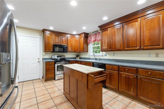 Kitchen featuring stainless steel appliances, light tile patterned floors, a center island, recessed lighting, and wood counters | Image 9