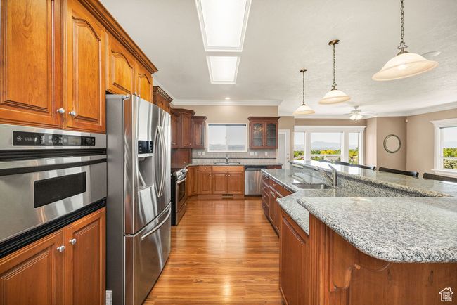 Kitchen featuring stainless steel appliances, a sink, brown cabinets, wood finished floors, and ornamental molding | Image 8