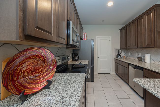 Kitchen featuring stainless steel appliances, backsplash, dark brown cabinetry, light tile patterned flooring, and recessed lighting | Image 17