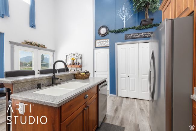 Kitchen with stainless steel appliances, a sink, a high ceiling, brown cabinetry, and light wood finished floors | Image 13