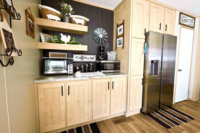 Kitchen with light brown cabinetry, wall chimney exhaust hood, appliances with stainless steel finishes, wood finished floors, and wooden walls | Image 4