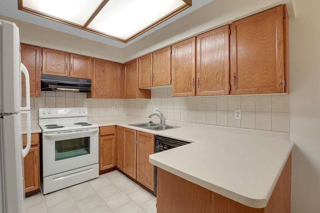 Kitchen featuring white appliances, ventilation hood, light countertops, backsplash, and brown cabinetry | Image 12