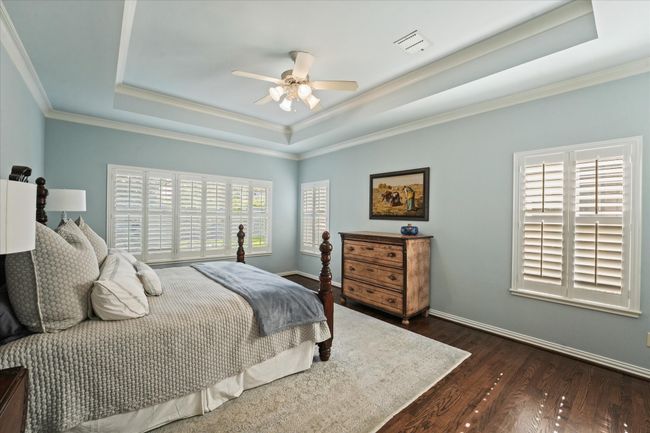 Bedroom featuring a raised ceiling, dark wood-style floors, crown molding, baseboards, and ceiling fan | Image 27