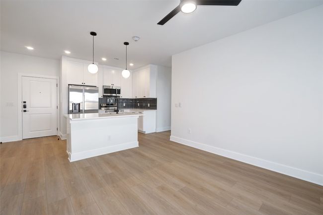 Kitchen with stainless steel appliances, light countertops, recessed lighting, a kitchen island with sink, and backsplash | Image 8