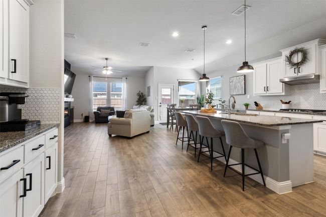 Kitchen featuring stone countertops, a breakfast bar, light wood-type flooring, under cabinet range hood, and a sink | Image 11