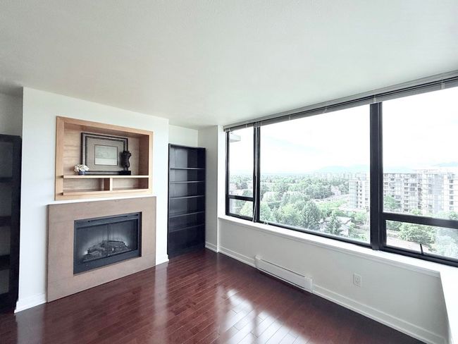 Unfurnished living room with baseboard heating, a fireplace, dark wood finished floors, and a city view | Image 9