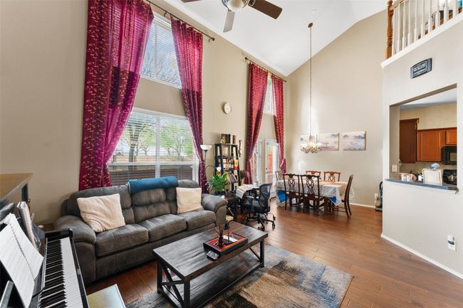 Living room featuring ceiling fan with notable chandelier, high vaulted ceiling, baseboards, and hardwood / wood-style flooring | Image 7
