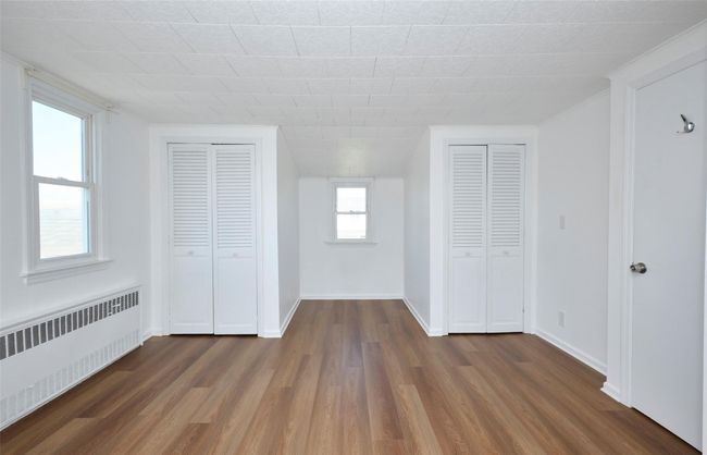 Unfurnished bedroom featuring radiator, multiple closets, dark wood-style floors, and baseboards | Image 18