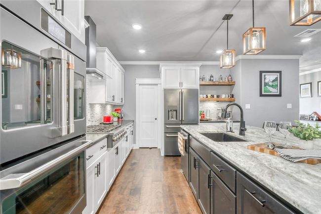 Kitchen featuring white cabinetry, sink, light stone counters, stainless steel appliances, and wall chimney exhaust hood | Image 16