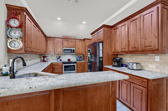 Kitchen featuring a sink, light stone countertops, brown cabinets, and appliances with stainless steel finishes | Image 13