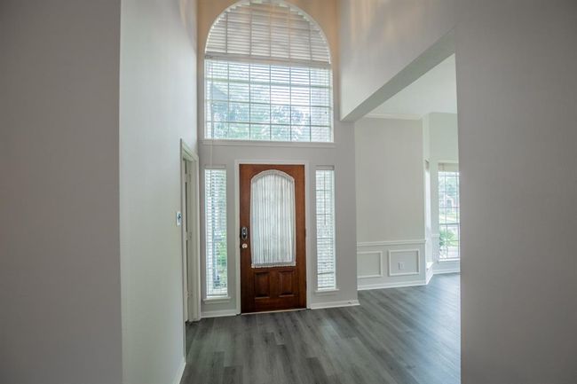 This entryway features a tall ceiling with an arched window above the door, allowing plenty of natural light. The space is accented with elegant wainscoting and modern flooring, offering a welcoming and stylish first impression. | Image 8