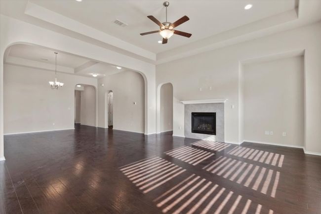 Unfurnished living room featuring a tray ceiling, dark wood-style floors, a fireplace, a ceiling fan, and a chandelier | Image 5