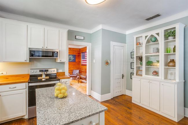 Kitchen featuring appliances with stainless steel finishes, white cabinetry, dark wood-style floors, ornamental molding, and butcher block countertops | Image 27