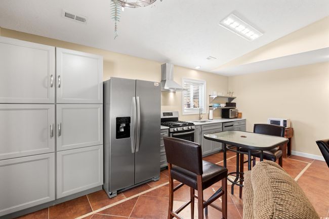 Kitchen featuring stainless steel appliances, wall chimney range hood, a sink, tile patterned flooring, and lofted ceiling | Image 21