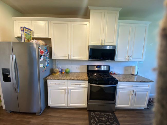 Kitchen with appliances with stainless steel finishes, decorative backsplash, dark wood-style floors, and white cabinets | Image 13