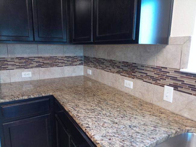 Kitchen featuring light stone counters, decorative backsplash, and dark cabinets | Image 4